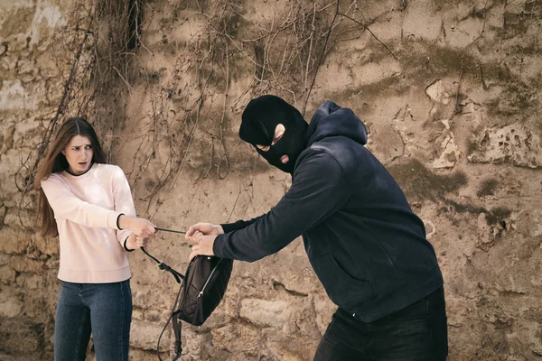 Homem mascarado a tentar roubar a mochila de uma mulher ao ar livre. Infracção penal — Fotografia de Stock