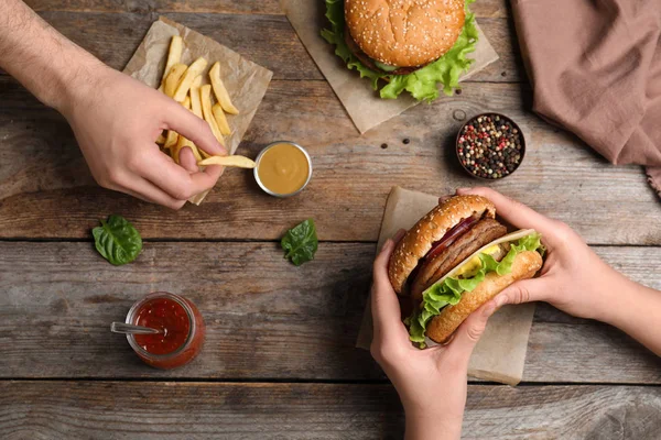 Pessoas com hambúrguer e batatas fritas na mesa de madeira, vista superior — Fotografia de Stock