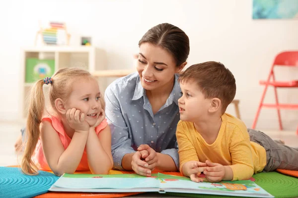 Professor de jardim de infância lendo livro para crianças dentro de casa. Aprendizagem e jogo — Fotografia de Stock
