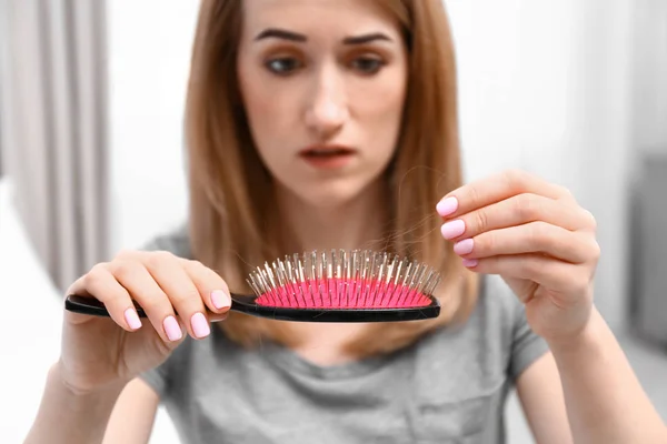 Emotional woman holding brush with fallen hair at home — Stock Photo, Image