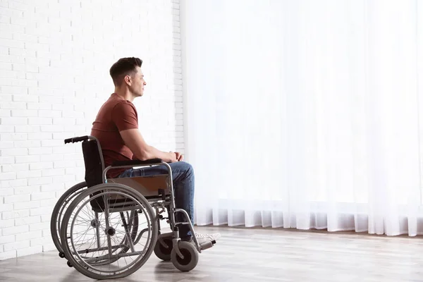 Задумчивый человек сидит в инвалидной коляске у окна дома — стоковое фото