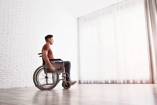 Задумчивый человек сидит в инвалидной коляске у окна дома — стоковое фото