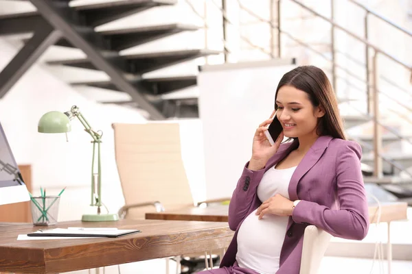 A fiatal terhes nő beszél telefonon, miközben dolgozik hivatalban — Stock Fotó