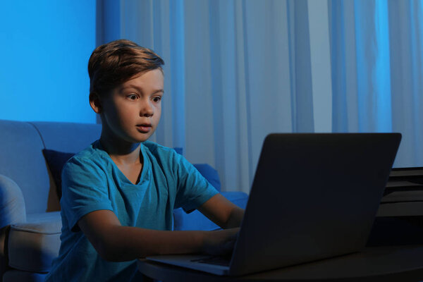 Потрясенный маленький ребенок с ноутбуком в темной комнате. Опасность интернета
