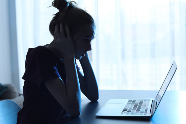 Terrified teenage girl with laptop at table indoors. Danger of internet