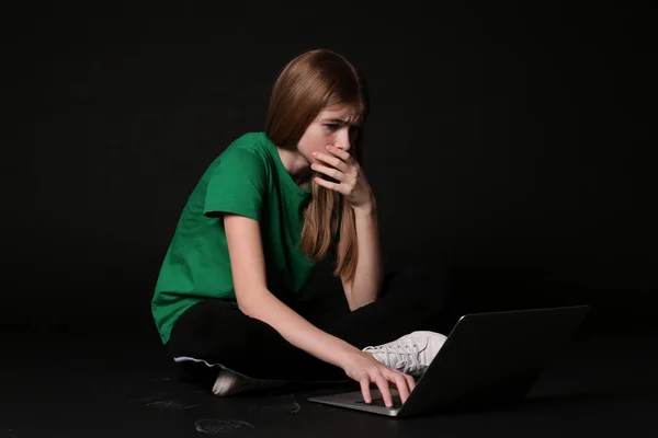 Ragazza adolescente terrorizzata con computer portatile su sfondo nero. Pericolo di internet — Foto Stock