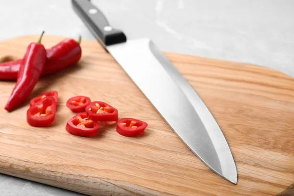 Wooden board with sharp knife and cut chili peppers on table, closeup