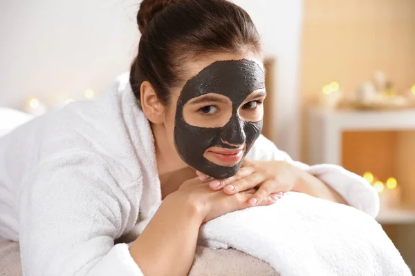 Hermosa mujer con máscara negra en la cara relajante en el salón de spa — Foto de Stock