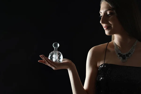 Mladá žena s lahví parfému na černém pozadí. Mezera pro text — Stock fotografie