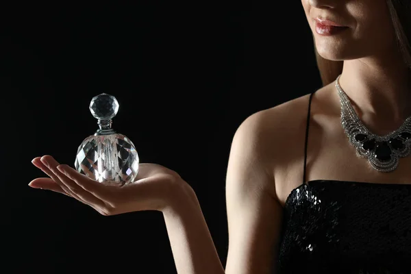 Siyah arka planda parfüm şişesi olan genç kadın, yakın plan. — Stok fotoğraf