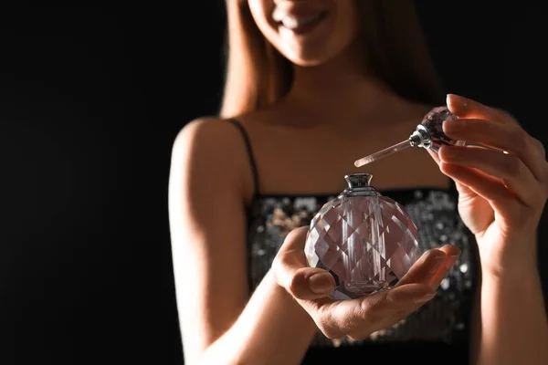 Young woman with bottle of perfume on black background, closeup. Space for text — Stock Photo, Image