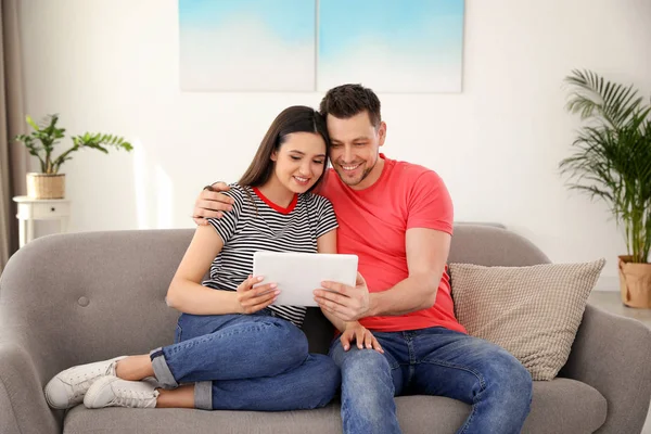 Pareja feliz con la tableta sentada en el sofá en casa — Foto de Stock