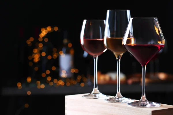 Vasos con diferentes vinos sobre mesa de madera contra luces desenfocadas. Espacio para texto — Foto de Stock