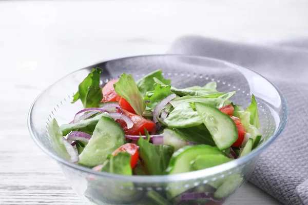 Schüssel mit schmackhaftem Salat mit Gurken, Tomaten und Salat auf dem Tisch — Stockfoto