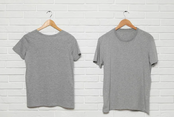 Appendini con t-shirt bianche su muro di mattoni bianchi. Finto per il design — Foto Stock