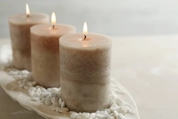Біла тарілка з трьома палаючими свічками та камінням на столі, простір для тексту — стокове фото