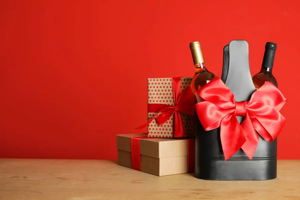 Weinflaschen im Halter mit Schleife und Geschenkschachteln auf dem Tisch vor farbigem Hintergrund. Raum für Text — Stockfoto