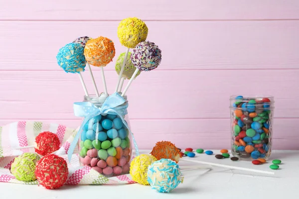 Yummy bright cake pops in glass jar full of candies on table. Space for text