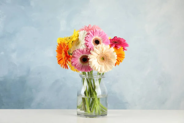 Csokor szép fényes Gerbera virágok üvegvázában asztal ellen, színes háttér — Stock Fotó