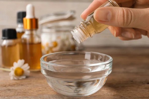 Mujer goteando aceite esencial en un tazón en la mesa, primer plano — Foto de Stock