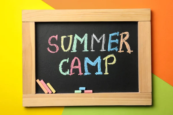 Kleine Tafel mit Text Sommerlager und Kreidestäbchen auf farbigem Hintergrund, Ansicht von oben — Stockfoto