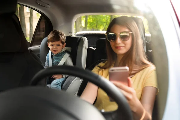 Madre usando el teléfono mientras conduce el coche con su hijo en el asiento trasero. Niño en peligro — Foto de Stock
