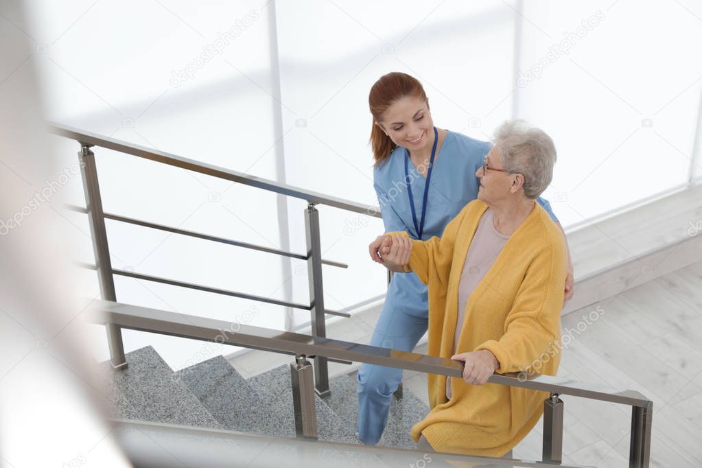 Nurse assisting senior woman to go up stairs at hospital