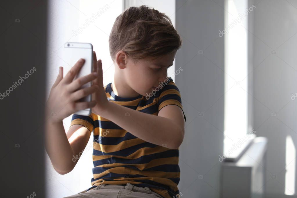 Frightened little child with smartphone indoors. Danger of internet
