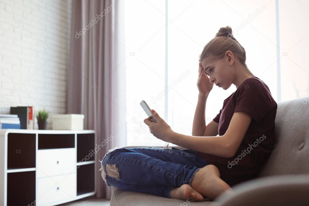 Upset teenage girl with smartphone in room. Danger of internet