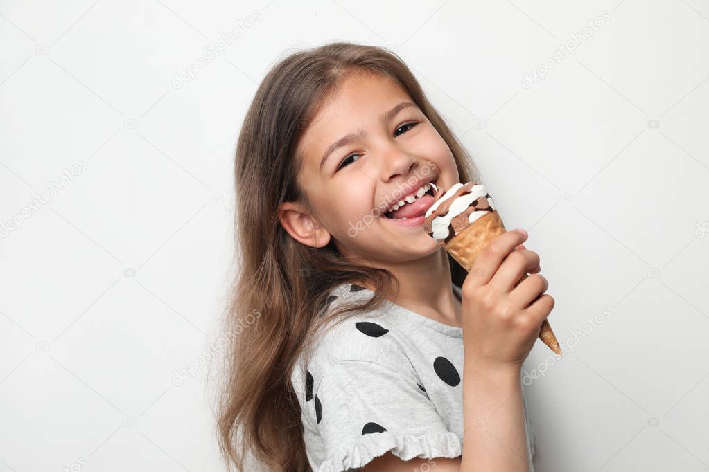 Adorable little girl with delicious ice cream against light background