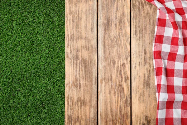 Picnic table with checkered cloth on grass, top view. Space for text