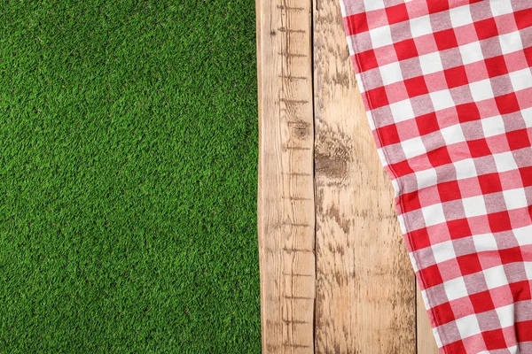 Picnic table with checkered cloth on grass, top view. Space for text