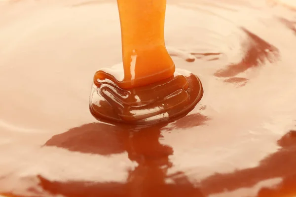 Despejando delicioso molho de caramelo como fundo, close-up — Fotografia de Stock