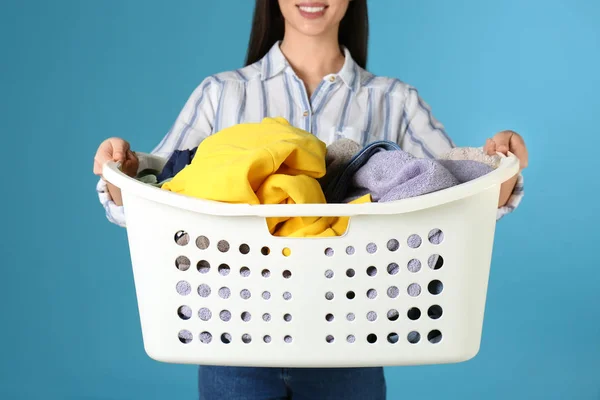 Young woman holding laundry basket with clothes on color background, closeup