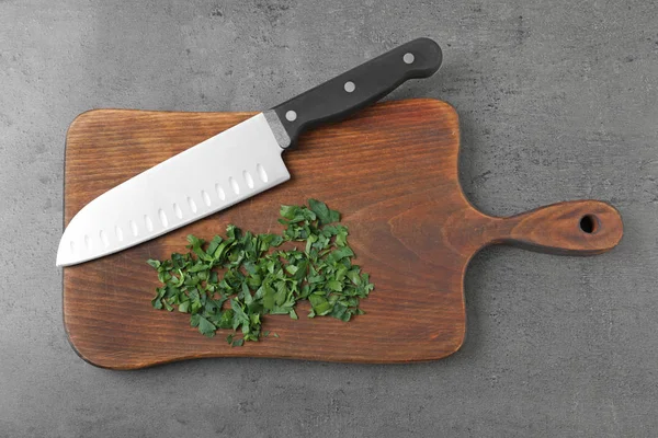 Tablero de madera con cuchillo afilado y perejil picado sobre fondo gris, vista superior — Foto de Stock