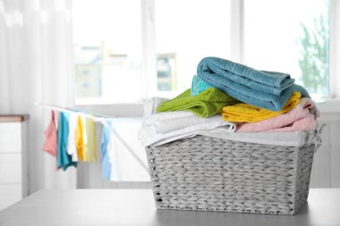 Basket with clean laundry on table at home, space for text clipart