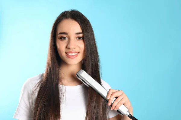 Mulher feliz usando ferro de cabelo no fundo de cor. Espaço para texto — Fotografia de Stock