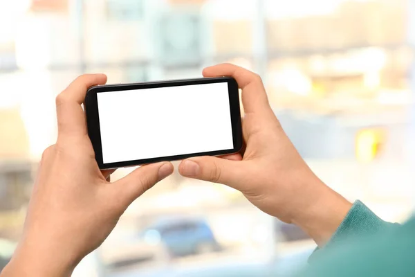 Mann hält Smartphone mit leerem Bildschirm auf verschwommenem Hintergrund, Nahaufnahme der Hände. Raum für Text — Stockfoto