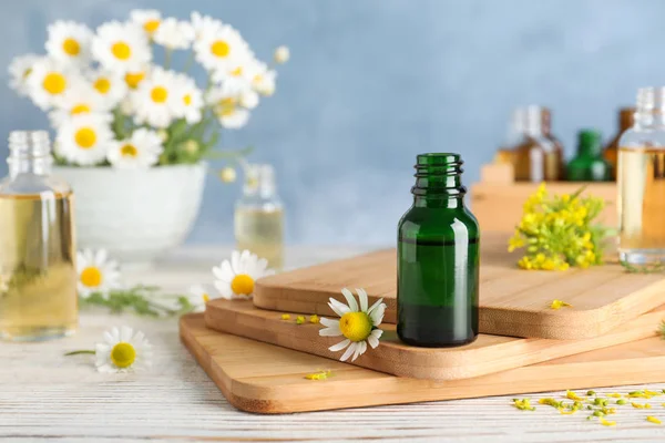 Láhev základního oleje a květin na dřevěném stole proti barevnému pozadí, prostor pro text — Stock fotografie