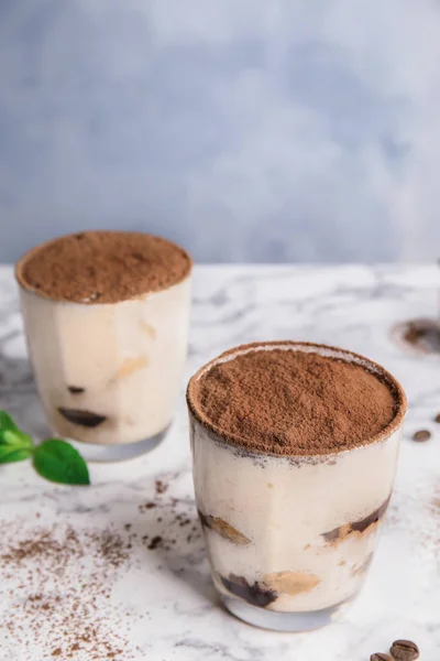 Two glasses of tiramisu cake on table against color background — Stock Photo, Image