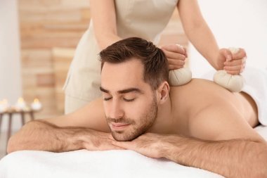 Spa salonunda bitkisel torba masajı alan yakışıklı adam