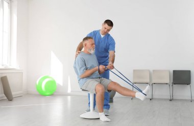 Professional physiotherapist working with senior patient in rehabilitation center clipart
