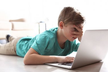 Kapalı yerde dizüstü bilgisayar ile korkmuş ve meraklı küçük çocuk. İnternet tehlikesi