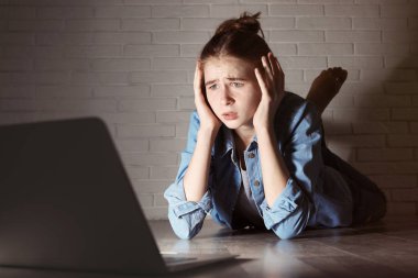 Karanlık odada yerde laptop ile şok genç kız. İnternet tehlikesi