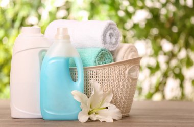 Clean towels in basket with lily and detergents on table against blurred background. Space for text clipart