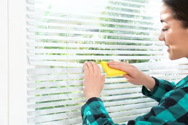 Genç kadın pencere jaluzi kapalı bez ile silerek. Temizlik öncesi ve sonrası — Stok fotoğraf