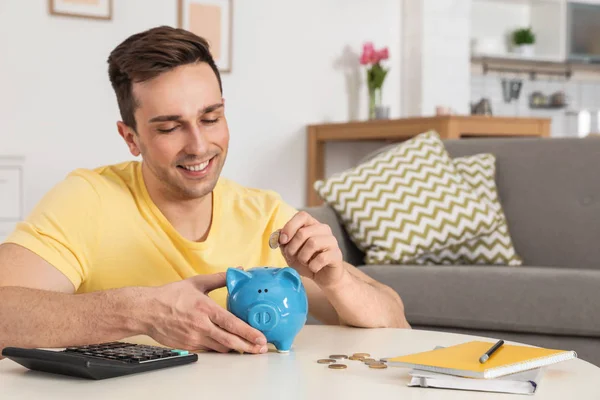 Gelukkige man zetten munt in Piggy Bank aan tafel in de woonkamer. Geld besparen — Stockfoto