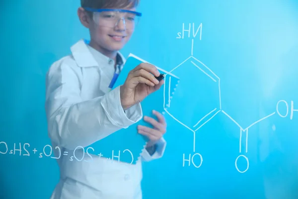 Schoolboy escrever fórmula química em placa de vidro contra fundo de cor. Espaço para texto — Fotografia de Stock