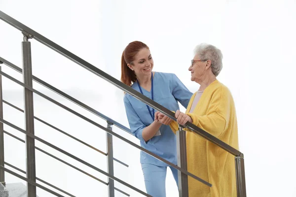 Nővér segíti idősebb nőt, hogy menjen fel a lépcsőn a kórházban — Stock Fotó