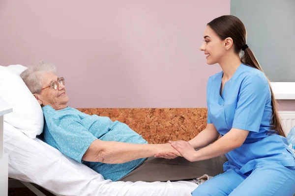 Enfermeira assistindo a mulher idosa deitada na cama na enfermaria do hospital — Fotografia de Stock